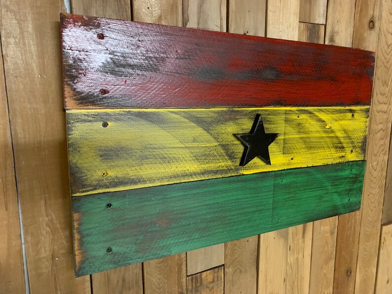 May include: A wooden sign painted in the colors of the Ghanaian flag. The sign is made of reclaimed wood and has a distressed look. The flag is red, yellow, and green with a black star in the center.