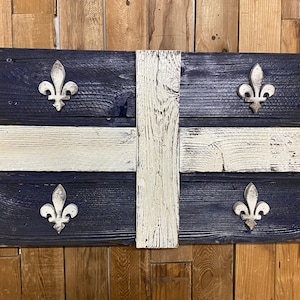 May include: A wooden sign featuring the flag of Quebec. The flag is blue with a white cross and four fleur-de-lis in the corners. The sign is made from reclaimed wood and has a rustic appearance.