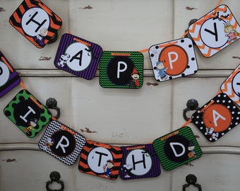 May include: A Halloween-themed birthday banner with orange, green, black, and purple squares. Each square features a different letter of the word "Happy Birthday" and a cartoon character from the Peanuts comic strip.