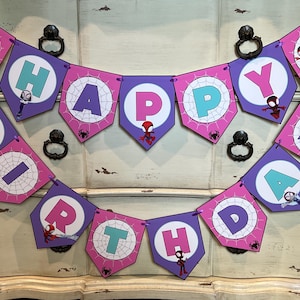 May include: A decorative banner spelling HAPPY BIRTHDAY with purple and pink pentagonal flags. Each flag features a white circle with a spiderweb pattern, a letter in teal or pink, and small illustrations of various Spider-Man characters.