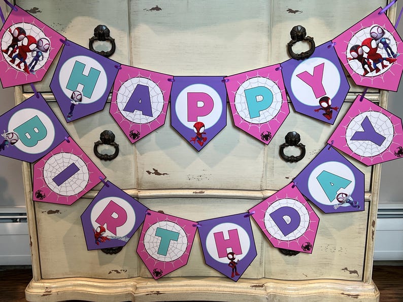 May include: A decorative banner spelling HAPPY BIRTHDAY with purple and pink pentagonal flags. Each flag features a white circle with a spiderweb pattern, a letter in teal or pink, and small illustrations of various Spider-Man characters.