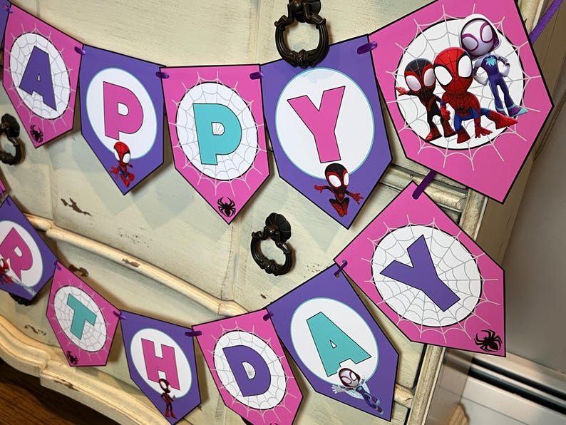 May include: A decorative banner spelling HAPPY BIRTHDAY with purple and pink pentagonal flags. Each flag features a white circle with a spiderweb pattern, a letter, and cartoon character illustrations of Spider-Man, Miles Morales, and Ghost-Spider.