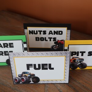 May include: Four table cards with monster truck graphics and text. The cards are labeled "Spare Tires", "Nuts and Bolts", "Pit Stop", and "Fuel".