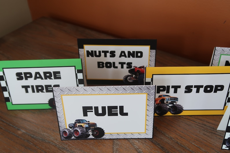 May include: Four table cards with monster truck graphics and text. The cards are labeled "Spare Tires", "Nuts and Bolts", "Pit Stop", and "Fuel".