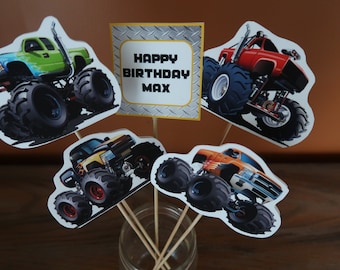 May include: Four monster truck cupcake toppers with a sign that says "Happy Birthday Max". The trucks are green, red, yellow, and orange.