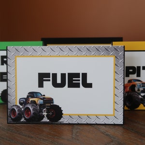 May include: Four table signs with monster truck graphics. The signs are labeled "Spare Tire", "Fuel", "Pit Stop", and "Monster Truck Party".