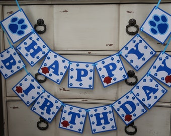May include: A blue and white banner with the words "Happy Birthday" in blue letters. The banner is decorated with paw prints and red dog bone shapes.