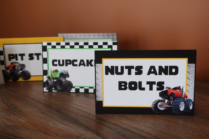 May include: Four monster truck themed food labels with black and yellow borders. The labels read "Pit Stop", "Cupcakes", and "Nuts and Bolts". Each label features a monster truck graphic.