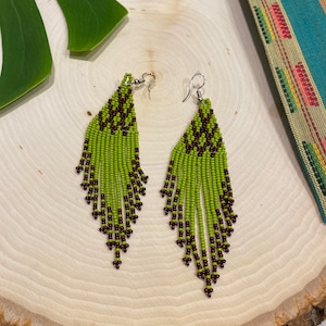 May include: A pair of long, green and brown beaded earrings. The earrings are made with small, round beads and have a fringe-like design.