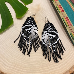 May include: A pair of black and white beaded earrings with a fringe design. The earrings are hanging from silver hooks.