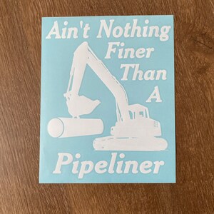 May include: White vinyl sticker with a blue background featuring a silhouette of an excavator digging a pipe. The text reads "Ain't Nothing Finer Than A  Pipeliner".