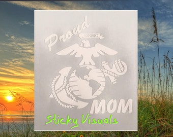 May include: White vinyl decal with the words "Proud Mom" and the USMC emblem. The emblem features a globe, an anchor, and an eagle with the words "USMC" above it. The decal is on a gray background.
