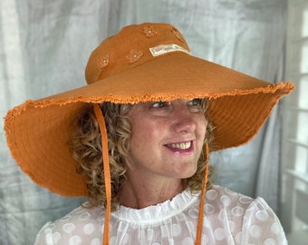 Burnt orange wide brimmed cotton sun hat featuring appliquéd flowers and string chin ties.