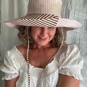 May include: A wide-brimmed sun hat with a brown and white striped brim and a pink and white patterned crown. The hat has a brown and white striped ribbon tied under the chin.