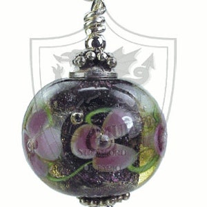 May include: A handcrafted glass bead pendant with a floral design. The bead is a dark purple color with pink flowers and green vines. The pendant is suspended from a silver chain. The text "Stratford Ontario" is visible on the bead.