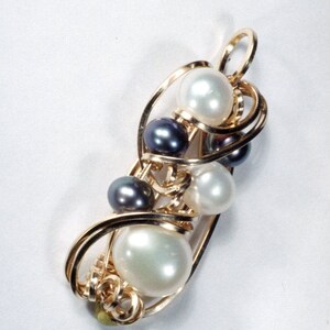 Peut inclure: Un pendentif doré avec un groupe de perles. Le pendentif présente un design en fil torsadé, avec des perles blanches et gris foncé. Les perles sont de tailles variées, et le pendentif a une boucle en haut pour une chaîne.