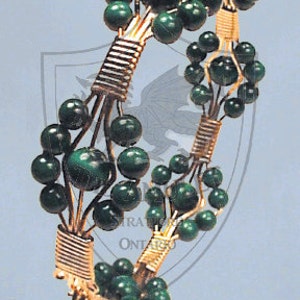 Puede incluir: Un brazalete de alambre dorado con cuentas de malaquita verde. Las cuentas están dispuestas en racimos y conectadas por alambre dorado. El brazalete es una pieza de joyería delicada e intrincada.