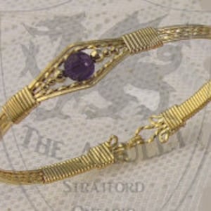 Könnte beinhalten: Ein goldfarbenes, drahtgewickeltes Armband mit einem violetten Amethyst-Edelstein in der Mitte.