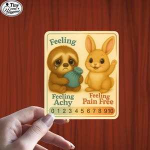 May include: A sticker featuring a sad sloth holding a blue bag and a happy bunny. The text reads "Feeling Achy" and "Feeling Pain Free" with a pain scale from 0 to 10. The sticker has the text "Tiny and Triggered" in the upper left corner.