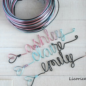 May include: A coil of multi-colored wire in black, pink, and light blue, alongside three wire-formed names: ashley in pink, claire in light blue, and emily in black. Each name features a small heart-shaped loop at the end. The text Licorice is visible.