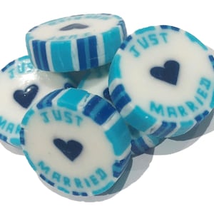 May include: A pile of round candies with a white center and blue striped edges. Each candy has the words "JUST MARRIED" around a dark blue heart. The candies are stacked on top of each other.
