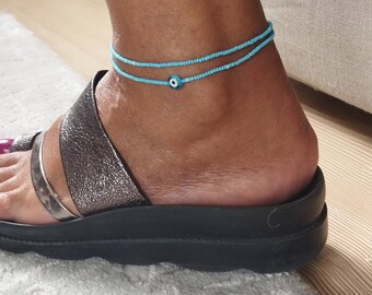 May include: A blue beaded anklet with an evil eye charm. The anklet is double-layered and has a light blue color.