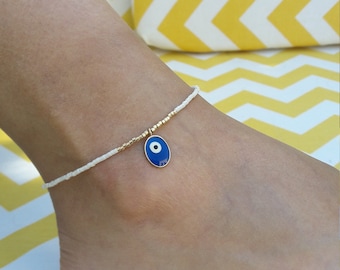 May include: White beaded ankle bracelet with a blue and white evil eye charm.