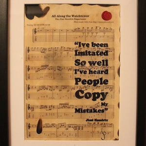 Op de afbeelding: Ingelijste bladmuziek print van "All Along the Watchtower" van Jimi Hendrix. De vintage print toont muzieknotatie en songtekst, inclusief de quote "I've been imitated so well I've heard people copy my mistakes". De print zit in een zwarte lijst.