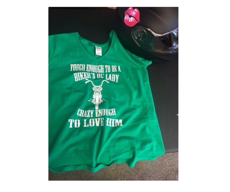 May include: Green t-shirt with a white graphic that says "Tough enough to be a biker's ol' lady, crazy enough to love him". The graphic also includes a motorcycle.