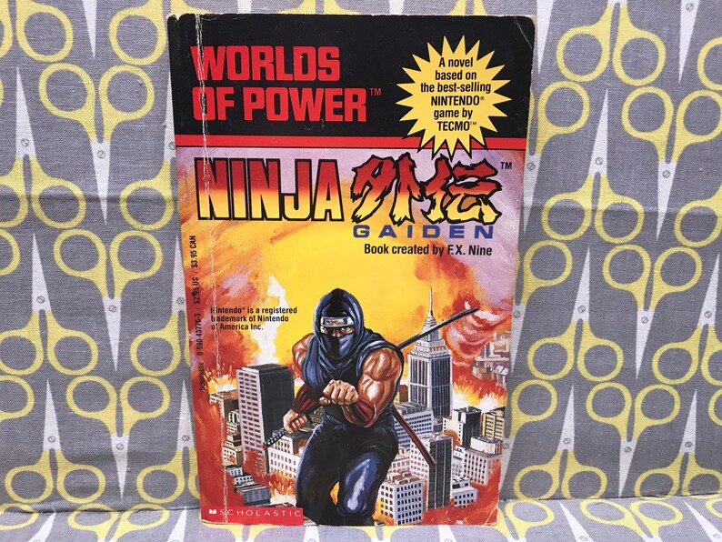 May include: A paperback book cover with a red, white, and blue illustration of a ninja character in a city setting. The book title is "Worlds of Power" and "Ninja Gaiden". The book is based on the Nintendo game by Tecmo.