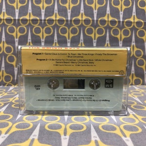 May include: A gold cassette tape with the title "The Very Best Of" and a list of Christmas songs. The tape is labeled "Program 1" and "Program 2" with the song titles listed below each program. The tape is manufactured by Capitol Records, Inc.