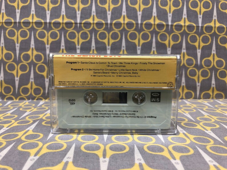 May include: A gold cassette tape with the title "The Very Best Of" and a list of Christmas songs. The tape is labeled "Program 1" and "Program 2" with the song titles listed below each program. The tape is manufactured by Capitol Records, Inc.