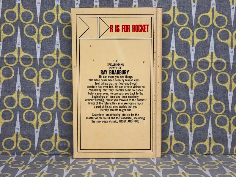 May include: A yellow and brown paperback book with the title "R is for Rocket" and the author "Ray Bradbury". The back cover features a description of the book, which includes the text "The Spellbinding Power of Ray Bradbury".