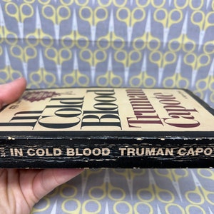 May include: A black paperback book with the title "In Cold Blood" by Truman Capote. The book is worn and has a few scratches on the cover.
