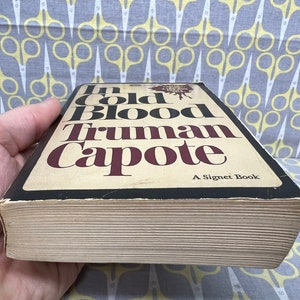 May include: A paperback copy of the book "In Cold Blood" by Truman Capote. The book cover is black with white and red text. The book is a Signet Book.