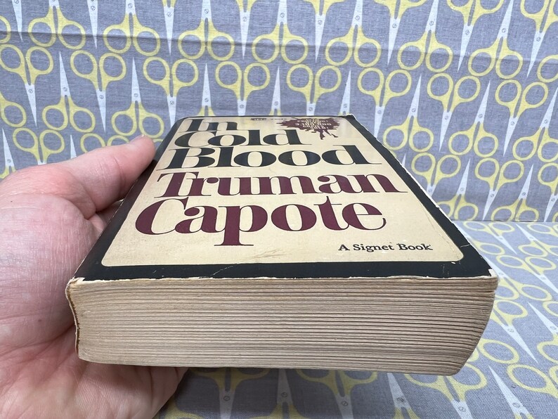 May include: A paperback copy of the book "In Cold Blood" by Truman Capote. The book cover is black with white and red text. The book is a Signet Book.