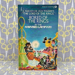 May include: Vintage paperback book titled "Bored of the Rings" by The Harvard Lampoon. The cover features a colorful illustration with fantasy characters and a hookah. The book is a parody of J.R.R. Tolkien's "The Lord of the Rings".