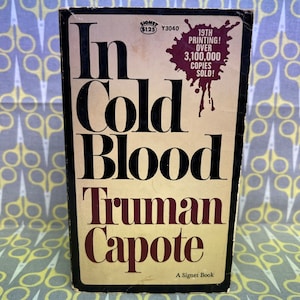 May include: A paperback book cover with a red splatter design. The title "In Cold Blood" is in large black letters. The author's name, "Truman Capote", is in red letters. The book is a Signet book and is the 19th printing with over 3,100,000 copies sold.