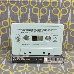 K&ouml;nnte beinhalten: Ein wei&szlig;es Kassettenband mit einem hellblauen Etikett. Das Etikett tr&auml;gt den Text "The Beatles Rock 'n' Roll Music Volume 1" und eine Liste von Songs. Das Kassettenband ist eine Neuauflage von Capitol Records.