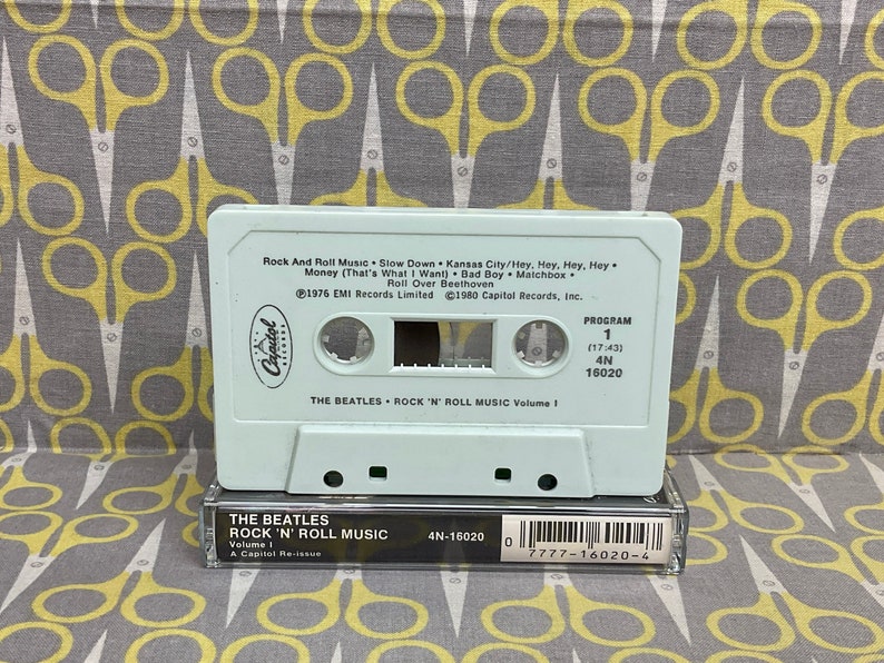 K&ouml;nnte beinhalten: Ein wei&szlig;es Kassettenband mit einem hellblauen Etikett. Das Etikett tr&auml;gt den Text "The Beatles Rock 'n' Roll Music Volume 1" und eine Liste von Songs. Das Kassettenband ist eine Neuauflage von Capitol Records.