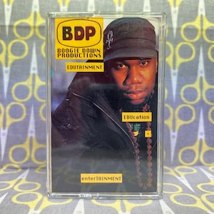 Könnte beinhalten: Ein Kassettenband mit einem Schwarzweißfoto eines Mannes mit einer schwarzen Kappe. Das Band ist mit "BDP Boogie Down Productions Edutrainment Education Entertainment" beschriftet.