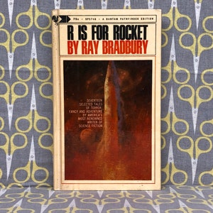 May include: A vintage paperback book cover with a white background and red and black text. The title is "R is for Rocket" by Ray Bradbury. The cover features a painting of a rocket ship against a red and orange background.