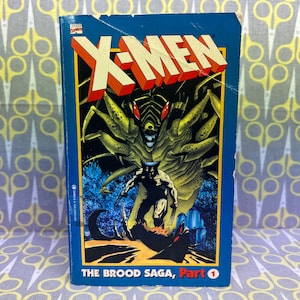 May include: A blue comic book cover with the title "X-Men" in red and yellow letters. The cover features a green, alien-like creature with a menacing expression and Wolverine, a superhero with claws, standing in front of it. The text "The Brood Saga, Part 1" is printed at the bottom of the cover.