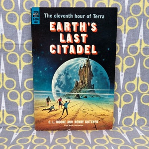 Op de afbeelding: Een vintage paperback boekomslag met een donkerblauwe achtergrond en een grote, heldere maan. De titel is "Earth's Last Citadel" in rode en witte letters. Het boek is van C.L. Moore en Henry Kuttner.