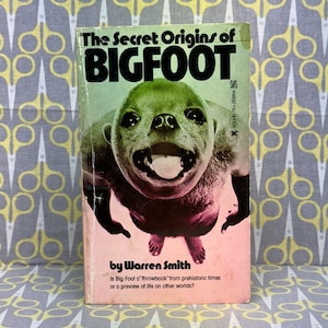 Op de afbeelding: Een vintage paperback boekomslag met een kleurrijke illustratie van een Bigfoot-wezen. De titel is "The Secret Origins of BIGFOOT" en de auteur is "Warren Smith". De tekst op de omslag luidt "Is Big Foot a 'throwback' from prehistoric times or a preview of life on other worlds?"