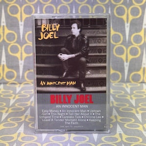Può includere: Una musicassetta vintage dell'album "An Innocent Man" di Billy Joel. La copertina presenta una foto in bianco e nero di Billy Joel. Il titolo dell'album e il nome dell'artista sono in grassetto. La tracklist è visibile.