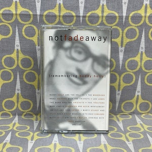 Puede incluir: Una cinta de casete blanca con una foto en blanco y negro de Buddy Holly en la parte delantera. El título "notfadeaway (remembering buddy holly)" está impreso en negro en la parte delantera de la cinta de casete. La cinta de casete enumera varios artistas, incluidos Buddy Holly and the Hollies, The Mavericks, Nanci Griffith with the Crickets, Los Lobos, The Band and the Crickets, The Tractors, Mary Chapin Carpenter and Kevin Montgomery, Joe Ely and Todd Snider,  Marth Stuart and Steve Earle, Suzy Bogguss with Dave Edmunds, Critte Gritty Dirt Band,  Watlon Jennings with Mark Knopfler, and  Dang Leno.