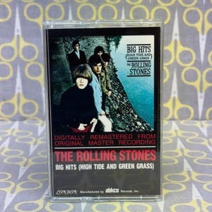 Op de afbeelding: Een vintage cassettebandje van het album "Big Hits (High Tide and Green Grass)" van The Rolling Stones. De hoes toont een bandfoto met de tekst "Digitally Remastered From Original Master Recording". De cassette zit in een doorzichtige plastic hoes.
