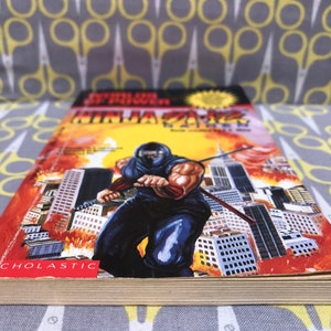 May include: A paperback book titled "Super Ninja" with a cover image of a ninja in a black suit holding a sword in front of a cityscape. The book is published by Scholastic.