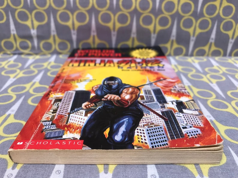 May include: A paperback book titled "Super Ninja" with a cover image of a ninja in a black suit holding a sword in front of a cityscape. The book is published by Scholastic.